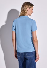 Ljusblå kortärmad polo med klassisk krage, slät yta och en ren design, kombinerad med mörkblå denimjeans.