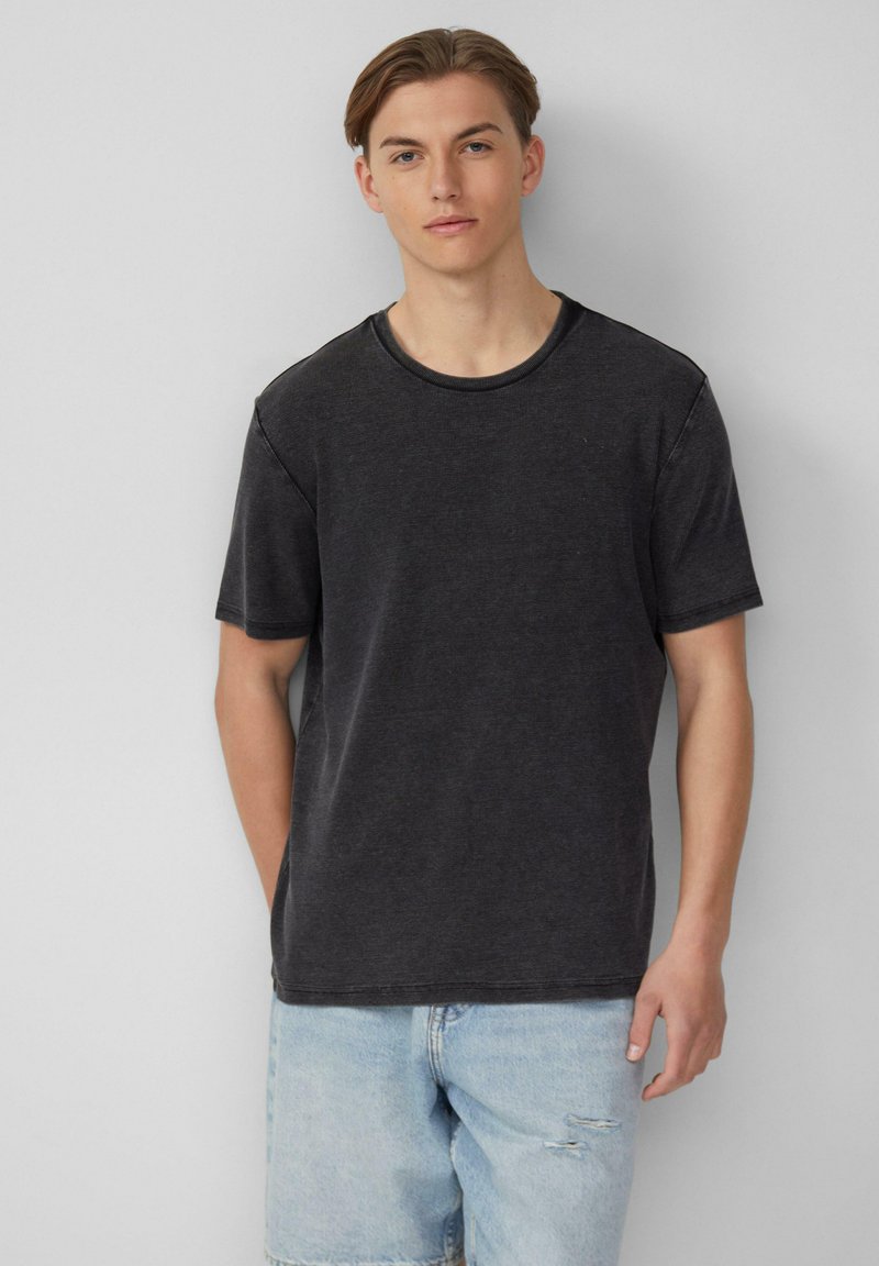 Zwarte katoenen t-shirt met een ronde halslijn en korte mouwen, met een gestructureerde afwerking. Draagt het met lichtblauwe denim shorts.