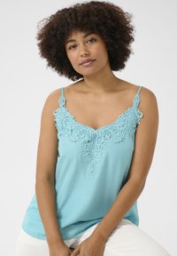 Šviesiai mėlynas marškinėlis be rankovių, papuoštas nėriniu aplink kaklą. Turi plonas petnešėles ir laisvą siluetą. Lygus paviršius, puikiai tinka sluoksniavimui.