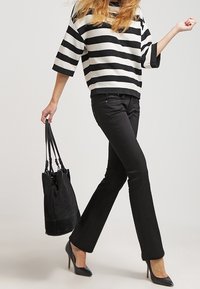 Pulóver texturizado a rayas blancas y negras con mangas anchas, combinado con pantalones de campana negros y zapatos de tacón altos negros; sosteniendo una bolsa de mano negra.