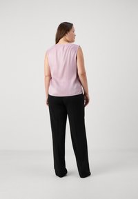 Lett rosa top uten ermer med rund hals, paret med svarte bukser. Glatt stoff og rett snitt. Ingen synlige detaljer eller teksturer.