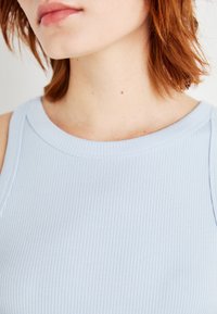 Ljusblå randig linne med vid halsringning, mjuk textur och sömlösa ärmhål, som visar subtila mönster och en figurnära design.