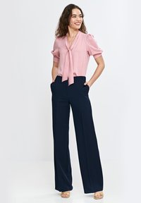 Jasnoróżowa bluzka z kokardą, w połączeniu z granatowymi spodniami o szerokich nogawkach. Gładki materiał, luźny krój oraz subtelnie bufiaste rękawy.