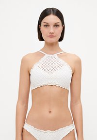 Biely háčkovaný bikiny s dizajnom na krku, s vlnkovanými okrajmi a textúrovaným vzorom. Zahrnuté sú aj zodpovedajúce nízkopásové spodné diely.