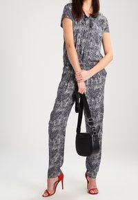 Niebieski i biały kombinezon w wzory z krótkimi rękawami, z wcięciem w talii; połączony z czarną torebką na ramię i czerwonymi sandałami na obcasie.