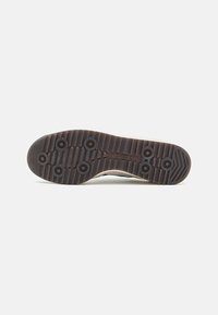 Suela de zapato Adidas con una superficie de goma texturizada, patrones de tracción circulares y una combinación de colores en tonos de marrón claro y marrón oscuro.