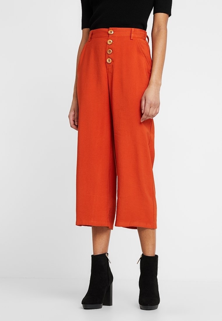 Roodbruin gekorte broek met een losse pasvorm, voorzien van een vijfknopen sluiting aan de voorkant en een soepele stof, gecombineerd met zwarte enkelboots.