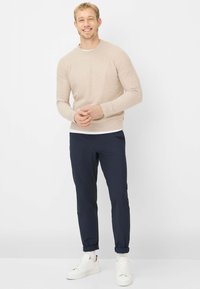 Maglione beige a maniche lunghe, pantaloni aderenti blu navy e sneakers bianche. Il maglione ha uno scollo tondo e una texture liscia; i pantaloni sono risvoltati ai polsini.