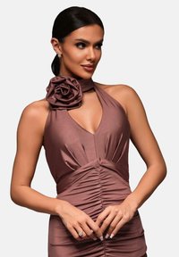 Abito a halter di colore lampone con applicazione floreale al collo, caratterizzato da una texture plissettata e una silhouette aderente, tessuto morbido e senza motivi.
