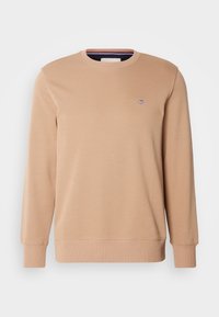 Sweat-shirt beige à manches longues col rond avec poignets et ourlet côtelés, avec un petit logo brodé sur le côté gauche de la poitrine.