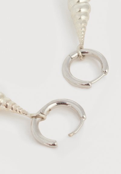 Ασημένια σκουλαρίκια κρίκοι με μοτίβα σε σχήμα σπειροειδούς κοχυλιού σε απλό λευκό φόντο, δείχνοντας τις ανοιχτές προσαρτήσεις των σκουλαρικιών.