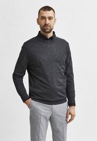 Dark grey knit sweater with a round neckline, worn over a black collared shirt. Paired with light grey tailored trousers, smooth texture.