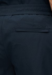 Λεπτομέρεια σκούρου ναυτικού μπλε παντελονιού με ελαστική μέση, μία πίσω τσέπη με γλώσσα και διακριτικό κεντημένο λογότυπο Calvin Klein πάνω από την τσέπη.