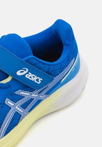 Baskets de sport bleues avec une tige en maille respirante, sangle Velcro, semelle blanche et accents jaunes clairs contrastants. Logo visible sur la sangle.