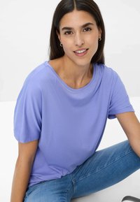 Lilla kortærmet t-shirt med rund hals og glat tekstur, båret med blå jeans. Enkel design, ingen synlige mønstre eller accenter.