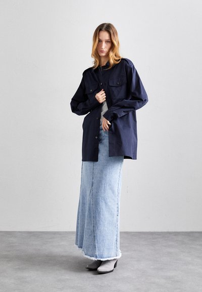 Marineblauwe oversized blouse met flapzakken, gecombineerd met een lichtblauwe denim maxi-rok en grijze enkellaarsjes. Soepele texturen, minimalistisch ontwerp.