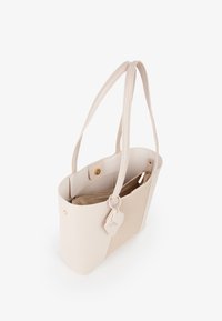 Borsa a spalla in pelle beige con manici lunghi, texture liscia, tasca interna con zip e un piccolo etichetta attaccata. Design minimalista con dettagli dorati.