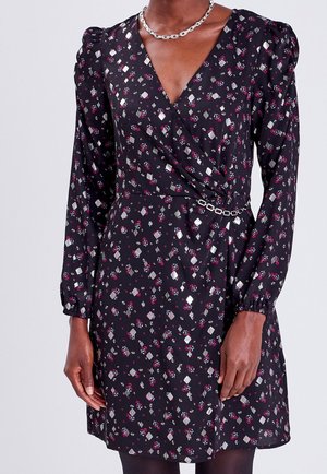 Robe portefeuille noire à manches longues avec motifs floraux et géométriques roses et argentés, épaules bouffantes, et ceinture chaîne argentée.