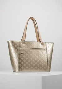 Zlatá syntetická taška na rameno s embosovanými květinovými vzory, dvě hnědé kožené uši a přední kapsou na zip. Hladká, lesklá textura.