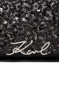 Schwarze Pailletten-Clutch mit silbernem Signatur-Logo. Die Oberfläche ist strukturiert mit kleinen, reflektierenden Pailletten in einem geometrischen Muster.