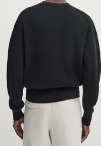 Black ribbed sweater with a rounded neckline, dropped shoulders, and a fitted waistband. Textured fabric with wide cuffs.