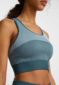 Teal sportbeha met verticale ribbels, een strakke pasvorm en brede bandjes. Het heeft een zachte textuur met een contrasterende band aan de onderkant.