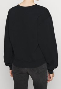 Sudadera negra de gran tamaño con cuello redondo, dobladillo de canalé y mangas con puños. La tela parece suave con una textura lisa.