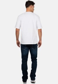 T-shirt bianco in cotone con maniche corte, abbinato a jeans in denim blu scuro. I jeans presentano un classico design a cinque tasche e cuciture sottili.