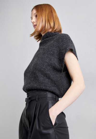 Σκούρο γκρι πλεκτό πουλόβερ με κοντά μανίκια και ψηλό λαιμό, σε συνδυασμό με μαύρο δερμάτινο παντελόνι ψηλής μέσης που διαθέτει ζώνη και τσέπες.