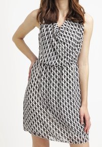 Utan ärm klänning i lättviktig tyg med ett svart och vitt mönster, i omslagsstil och med samlad midja.