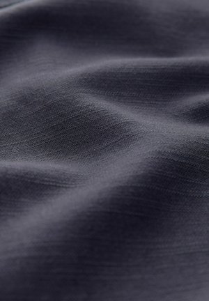 Tummanharmaa kangas, jossa on sileä, hieman teksturoitu pinta, jossa on hienovaraisia poimuja ja valon vaihteluita materiaalin pinnalla.