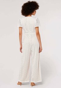 White lace jumpsuit featuring short puff sleeves, a high waist, wide-leg design, and intricate geometric patterns throughout.