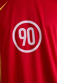 Rød sports trøje med et cirkulært hvidt logo og nummeret "90" i fed skrift, lavet af let, struktureret stof.