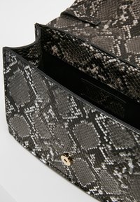 Pequeño bolso rectangular con un patrón de piel de serpiente en gris y negro, tapa abierta y cierre de torsión dorado sobre una superficie blanca.