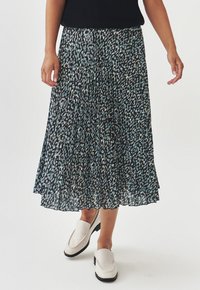 Jupe plissée noire avec un motif à pois bleu et blanc, fabriquée en tissu léger, associée à des chaussures à enfiler de couleur claire.