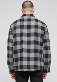 Languota striukė su juodais ir pilkais blokais, užsegamas apykaklės tipo užkabinamas užtrauktukas, ilgomis rankovėmis ir tekstūruotu audinio paviršiumi. Rodomas nugaros vaizdas.