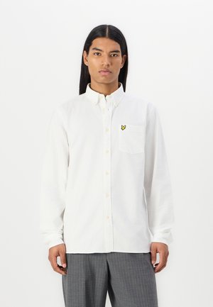 White button-up shirt made of cotton, featuring a chest pocket and a yellow embroidered logo. Long sleeves with button cuffs.