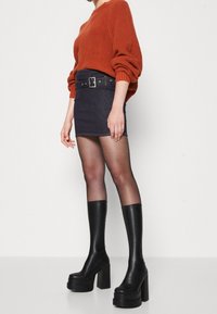 Maglione a coste color ruggine, mini gonna in denim scuro con cintura nera, collant trasparenti e stivali neri alti fino al ginocchio con plateau.