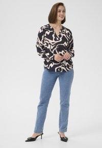 Bluse med lange ærmer i et sort og beige abstrakt mønster, V-udskæring, parret med lyseblå jeans og sorte hælede mules.