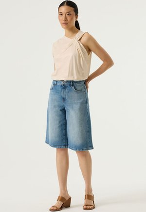 Beige mouwloze top met gedraaide ontwerp; lichtblauwe denim shorts met een losse pasvorm; bruine sleehakken. Eenvoudige en casual outfit.