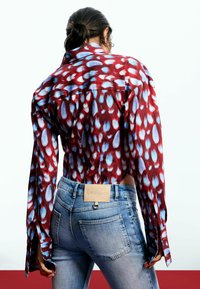 Cămașă cu mâneci lungi, cu model roșu și albastru, cu guler, asortată cu blugi strâmți de culoare albastru deschis, cu o etichetă pe talie.