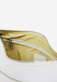 Innerraum einer weißen Lederhandtasche mit glatter Textur, kontrastierender gelber Fütterung und einem Reißverschlussteil, um kleinere Gegenstände zu halten. Silberne Reißverschlussbeschläge.