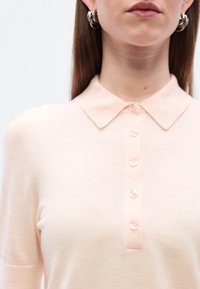 Ανοιχτό ροζ πόλο πουκάμισο με κλασικό γιακά, επταπλή σειρά κουμπιών και απαλή υφή. Τα κουμπιά  είναι στο χρώμα του υφάσματος.