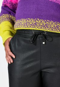 Pantaloni jogger neri in pelle con una texture liscia e cintura elastica, dotati di cordino e dettagli in metallo argentato.
