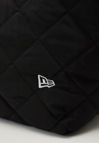 Tecido acolchoado preto com um padrão em diamante, apresentando um detalhe do logo bordado em branco de um lado. Textura suave e acabamento macio.