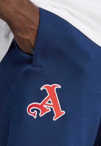 Marineblå sweatpants med et rødt broderet bogstav "A" på venstre side, der har en glat tekstur og en sidelomme.