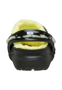 Zoccoli neri senza lacci con rivestimento in pile giallo e cinturino posteriore regolabile, mostrati da dietro.