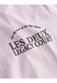 Light pink cotton fabric featuring bold black text that reads "LES DEUX LEGACY COURT" and a curved message above in smaller font.