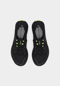 Ζευγάρι μαύρα αθλητικά παπούτσια με νέον πράσινες λεπτομέρειες, επάνω μέρος από δίχτυ και γκρι εσωτερικές σόλες με την επωνυμία "MINIMUS", φωτογραφημένα από πάνω.