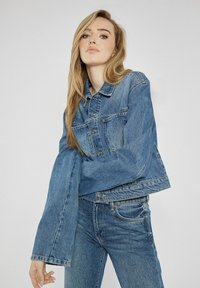 Jeansowa kurtka o skróconym kroju, z przodem na guziki, szerokimi rękawami i wyblakłym niebieskim kolorze. Połączona z dopasowanymi, przetartymi dżinsami.